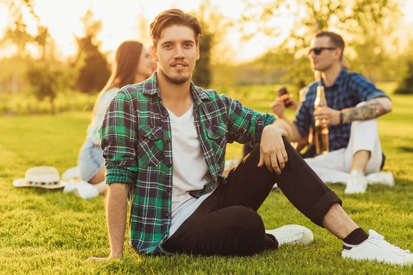 迷人的年轻人 穿着休闲装 和他的朋友们一起休息 坐在草坪上野餐 在公园里野餐 夏天野餐 — 图库照片