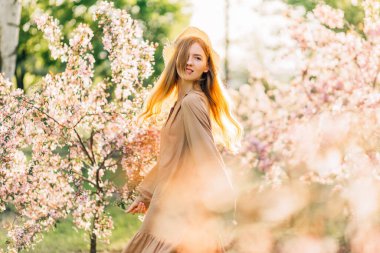 Genç bir kadın yeşil bir parkta yürür ve baharın tadını çıkarır. Çiçekleri açan bir kadın güneşli bir günde bir bahar parkında.