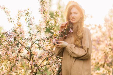 Kirazlı sakura çiçekleri içinde güzel bir kadın. Gülümseyen bir kadın. Pembe çiçeklerle çiçek açan ağacın yanında poz veriyor.