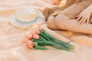 Güzel, gülümseyen genç bir kadın, bir buket lale ile, parktaki çimlerin üzerinde, güneşli bir yaz gününde, doğanın tadını çıkarıyor.