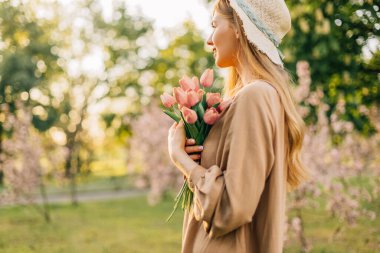 Güzel, genç, gülümseyen bir kadın, yaz hasır şapkasıyla, baharda bir meyve bahçesinde, çiçek açan bir bahçede, gün batımında.
