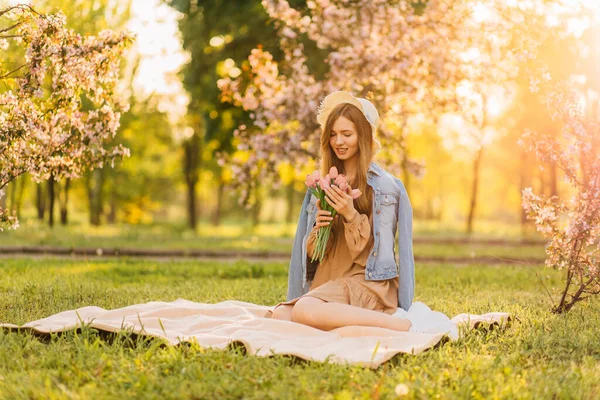 一个戴着帽子的年轻漂亮的女人 带着一束春天的郁金香 在大自然中 在公园的草地上野餐 在夏天 — 图库照片