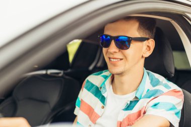 Güneş gözlüklü yakışıklı genç adam, yeni arabasını kullanan gülümseyen adam, araba kullanırken gülümseyen, hareket halindeki başarı.