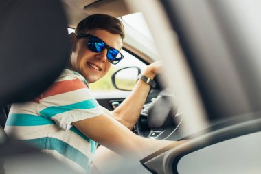 Güneş gözlüklü yakışıklı genç adam, yeni arabasını kullanan gülümseyen adam, araba kullanırken gülümseyen, hareket halindeki başarı.