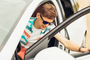 Güneş gözlüklü, yaz elbiseli, arabasının yanında duran, yaz günbatımının tadını çıkaran genç adam, seyahat konsepti.