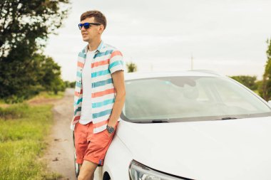 Güneş gözlüklü yakışıklı, beyaz arabasının yanında, arabanın arka planında yakışıklı, dışarıda, yolda.