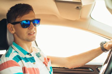 Mutlu erkek sürücü gülümsüyor, genç adam açık camlı arabada otururken arabasını sürüyor.