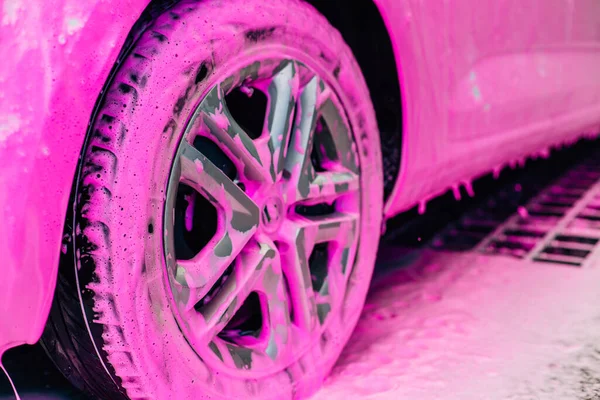 Car wash concept, Front view of white sports car covered with pink foam, Professional cleaning and car wash