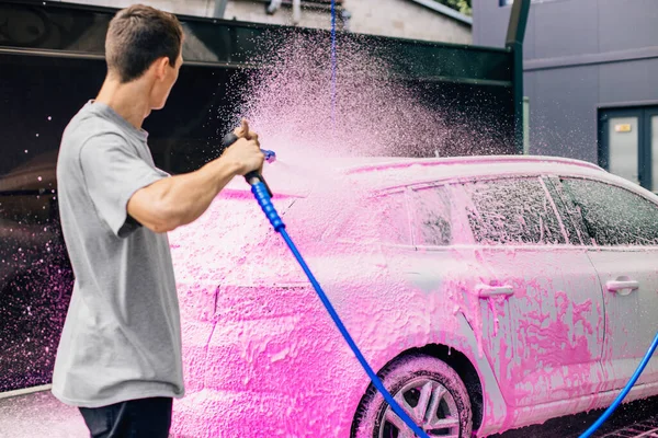 Car wash with soap, Car cleaning with high pressure water, a man washes the car, washes off the foam with water
