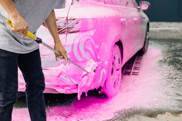 Car wash concept, Front view of white sports car covered with pink foam, Professional cleaning and car wash, Man washing car with high pressure water