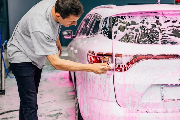 Detailed view of a car wash, car wash with foam, a man washes the headlights of a car with a special brush, an automatic car wash in action