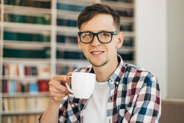 Gülümseyen, gözlüklü genç bir adam bir iş molasında kahve içiyor modern bir restoranda genç ve zeki bir adam bir kafede dinleniyor.