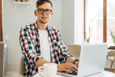 Evde dizüstü bilgisayarla çalışan gözlüklü genç bir iş adamı, ofisinde kahve ile oturan genç bir adam.