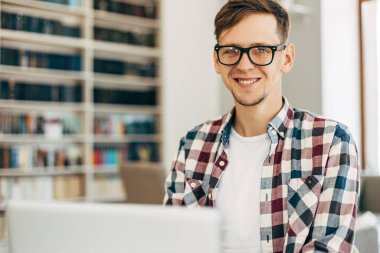 İş gözlüklü genç bir adam, bir kafede bir masada oturuyor ve dizüstü bilgisayarda çalışıyor, aromatik kahve içiyor, blogu için yeni içerikler yaratıyor, serbest çalışan birinin çalışmalarından zevk alıyor.