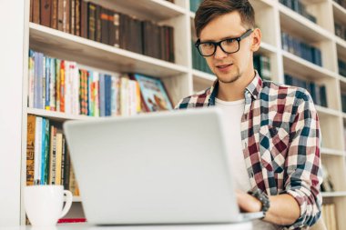 Çekici erkek işçi kafeteryada bilgisayar kullanıyor, genç adam dizüstü bilgisayar kullanıyor.