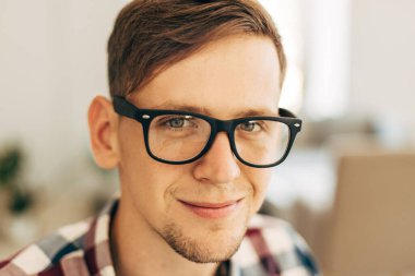 Gözlüklü ve ekose gömlekli mutlu bir gencin portresi. Gülümseyen ve kameraya bakan mutlu bir adam.