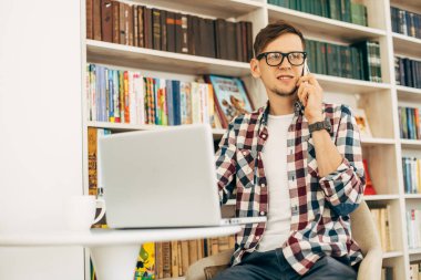 Gülümseyen, şık, gözlüklü genç bir erkek öğrenci, dizüstü bilgisayar kullanan ve cep telefonuyla konuşan başarılı bir adam, kütüphanede kitaplarla arka planda okuyan bir öğrenci.
