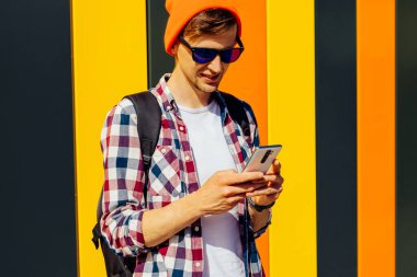 Güneş gözlüklü ve şapkalı genç bir hippinin portresi. Caddede yürüyen ve telefonda konuşurken yüzünü çeviren gülümseyen bir adam. Şehirdeki renkli bir duvarın arkasında.