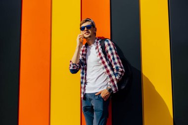 Güneş gözlüklü ve şapkalı genç bir hippinin portresi. Caddede yürüyen ve telefonda konuşurken yüzünü çeviren gülümseyen bir adam. Şehirdeki renkli bir duvarın arkasında.