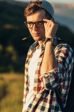 Genç ve yakışıklı bir adamın portresi, gözlüklü ve şapkalı, gülümseyen genç bir adam, güzel bir ormanın arka planında, sokakta dikiliyor.