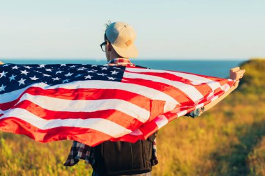 Amerika bayrağı taşıyan bir gezgin, sırt çantalı bir adam, denizin arka planında, açık havada bir adam, Amerikan bayrağı, vatansever bayrağı,