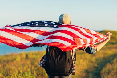 Amerika bayrağı taşıyan bir gezgin, sırt çantalı bir adam, denizin arka planında, açık havada bir adam, Amerikan bayrağı, vatansever bayrağı,