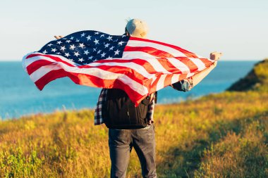 Amerika bayrağı taşıyan bir gezgin, sırt çantalı bir adam, denizin arka planında, açık havada bir adam, Amerikan bayrağı, vatansever bayrağı,