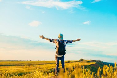 Elleri havada bir gezgin yeşil çimlerde bir tepede duruyor ve görkemli bir günbatımının tadını çıkarıyor zaferin tadını çıkaran başarılı bir adam, spor ve başarı kavramı, seyahat...
