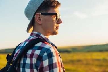 Sırt çantalı genç adam, yazın doğayı keşfeder, tepeleri ve tepeleri gezer, büyük bir sırt çantasıyla gezer, ormanlarda gezer, yaz manzarası