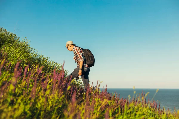 Young tourist, a man with a backpack, hikes, hiking in the mountains, a tourist with a backpack, looking into the mountains. Smiling guy, active healthy lifestyle, adventure travel, vacation