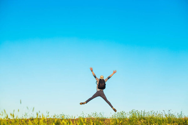 Rear view of man jumping up with outstretched arms, happy man with arms up against blue sky background, outdoors, concept of travel, nature, freedom