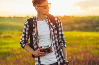 Genç erkek turist, güneş gözlüklü, kameralı, doğa yürüyüşü yapan, sahada zaman geçiren seyahat konsepti, turizm, yürüyüş