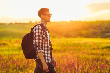 Sırt çantalı genç bir adam, çimde kır çiçekleriyle, arka planda Zakta 'nın, seyahat, doğa, turizm, orman kavramına karşı.