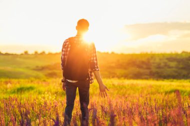 Sırt çantalı genç bir adam, çimde kır çiçekleriyle, arka planda Zakta 'nın, seyahat, doğa, turizm, orman kavramına karşı.
