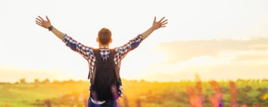 Elleri havada bir gezgin yeşil çimlerde bir tepede duruyor ve görkemli bir günbatımının tadını çıkarıyor zaferin tadını çıkaran başarılı bir adam, spor ve başarı kavramı, seyahat...