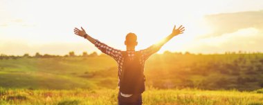 Elleri havada bir gezgin yeşil çimlerde bir tepede duruyor ve görkemli bir günbatımının tadını çıkarıyor zaferin tadını çıkaran başarılı bir adam, spor ve başarı kavramı, seyahat...