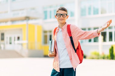 Gözlüklü, sırt çantalı, kitaplı, mutlu bir çocuğun portresi okula gidiyor, yaz tatillerinden sonraki yıl yeni bir okula başlıyor.