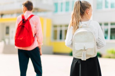 Sırt çantalı iki çocuk okula gidiyor, erkek ve kız öğrenciler, okul arkasında okul çantaları olan çocuklar, karantinadan sonra okula dönüyorlar.