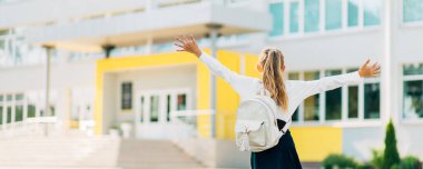 Çantalı mutlu kız öğrenci, okulun arka planında atlayan okul çocuğu, okul eğitimi ve insanların konsepti.