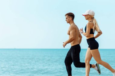 Plajda koşan genç bir çift, sportif çekici insanlar yaz sporu kıyafetleriyle, deniz kıyısında koşuyorlar, sağlıklı yaşam tarzlarını geliştiriyorlar.