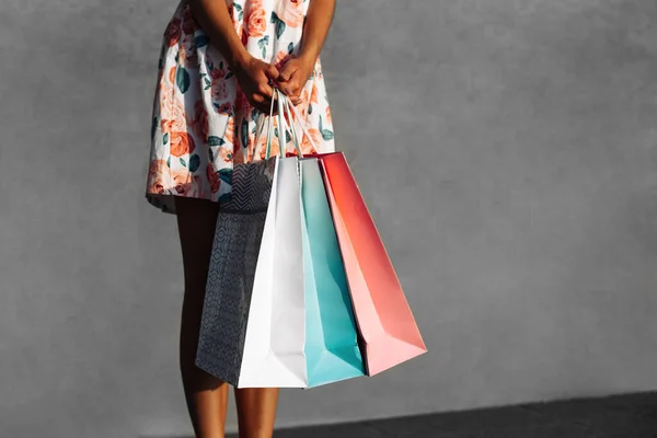 Happy shopping, Cropped view of woman holding shopping bags, woman in bright summer dress holding colorful bags, against gray wall in city, shopping concept, summer sale, consumerism