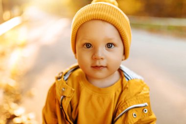Sonbaharda açık havada sarı yapraklı, sıcak renkli giysiler içinde gülümseyen çocuk, sonbaharda sarı şapkalı ve ceketli küçük çocuk.