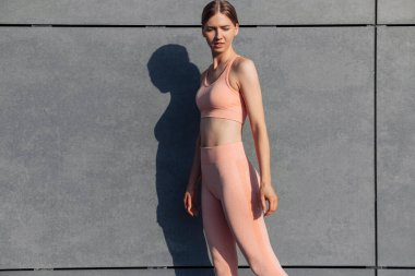 Fitness sporcusu kadın, moda sporlarında, sokakta yoga egzersizleri yapıyor, arka planda şehir gri duvarları, açık hava sporları, şehir tarzı.