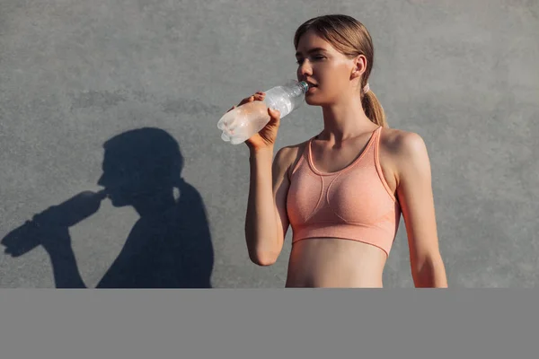 Sportive young woman, in sportswear, standing near the wall outdoors, Sportive woman with a bottle of water relaxing after training, sports, motivation