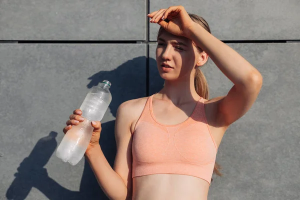 Sportive young woman, in sportswear, standing near the wall outdoors, Sportive woman with a bottle of water relaxing after training, sports, motivation