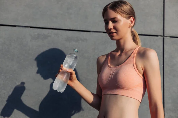 Sportive young woman, in sportswear, standing near the wall outdoors, Sportive woman with a bottle of water relaxing after training, sports, motivation