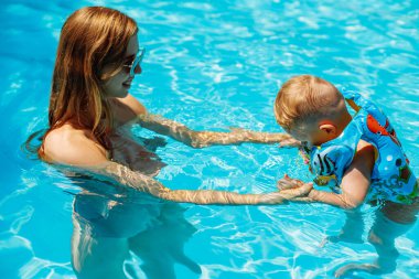 Mutlu aile, anne ve bebek şişme yelek içinde yüzüyor ve havuzda eğleniyor, aile tatilinde suda eğleniyor, yaz tatili kavramında, ailede.