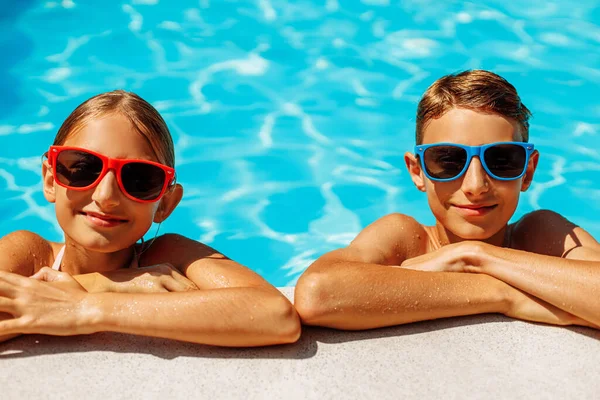 Happy kids in the pool, Funny kids in sunglasses playing outdoors, little boy and girl swim in the pool on a summer sunny day, Summer holiday concept