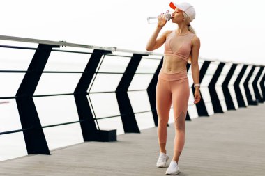 Güzel bir kadın koşucunun dışarıda elinde bir şişe su tutarken, spor yapan bir kadının köprüdeki antrenmandan sonra mola verirken görüntüsü.