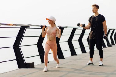 Fit genç çift kettlebell çömelmesi yapıyor, sportif kaslı erkek ve kadın gün doğumunda açık havada egzersiz yapıyor, sağlıklı yaşam tarzı, spor